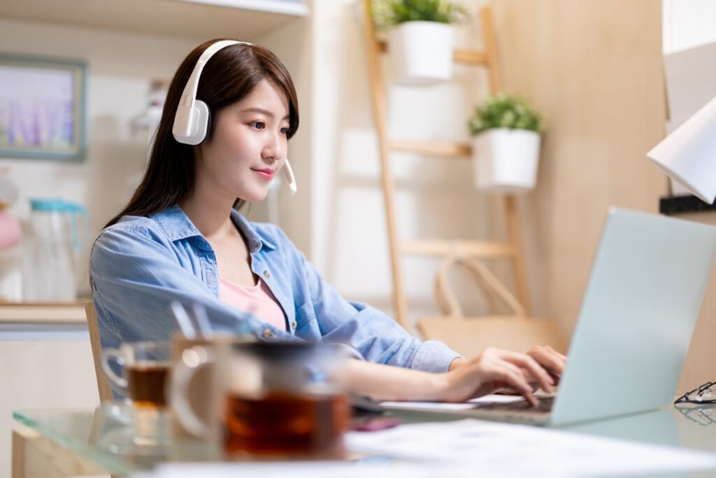 Young woman wearing a headset while working on a laptop at home, representing customer service or virtual assistant remote jobs for beginners with no experience.