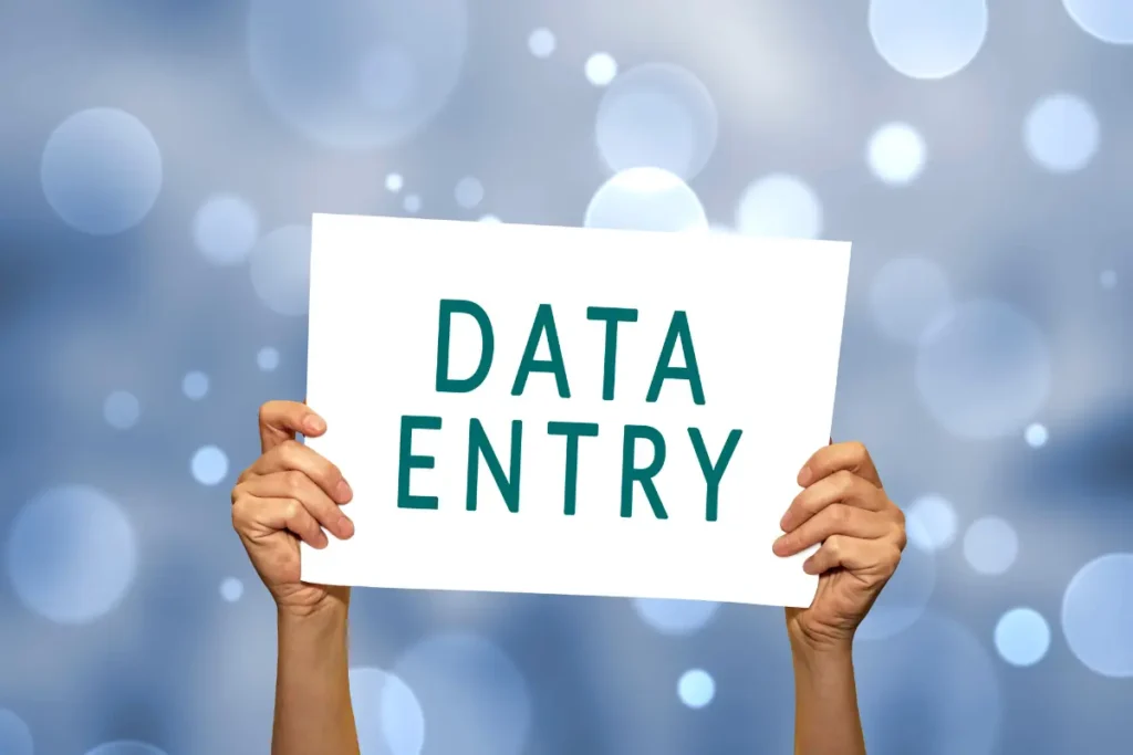 Two hands holding up a white sign with the words “DATA ENTRY” written in bold green letters against a soft blue background with light bokeh effects, symbolizing online data entry jobs for beginners.
